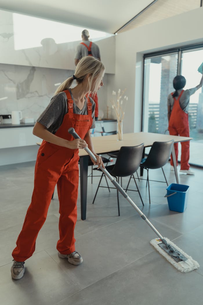 services-04 Cleaning team in red overalls mopping and sanitizing a modern home interior.