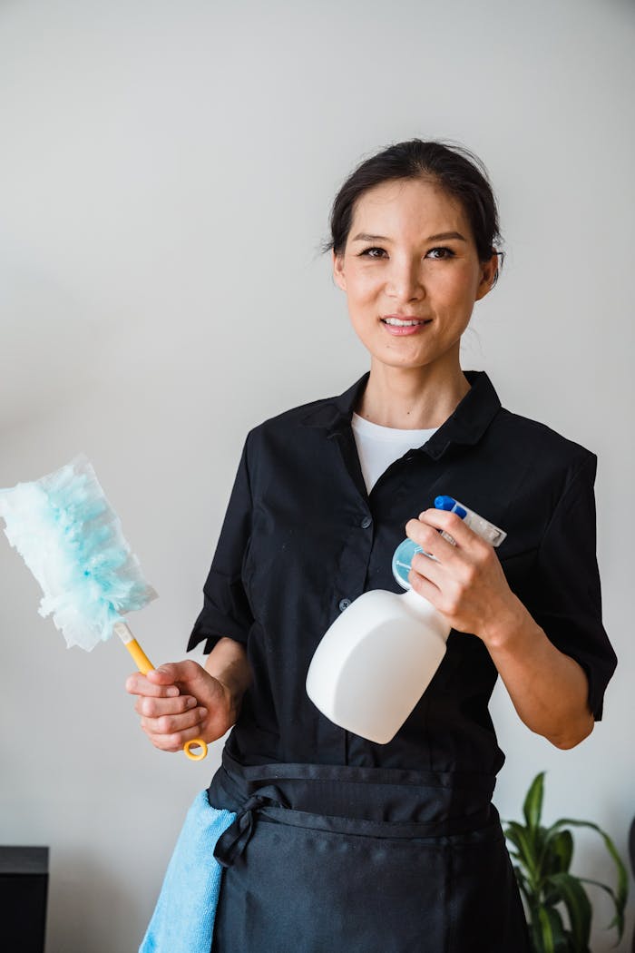 The Art of Drawing Readers In: Your attractive post title goes here A female housekeeper smiling while holding cleaning tools indoor.